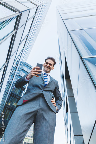 businessman stands with a phone between skyscrapers