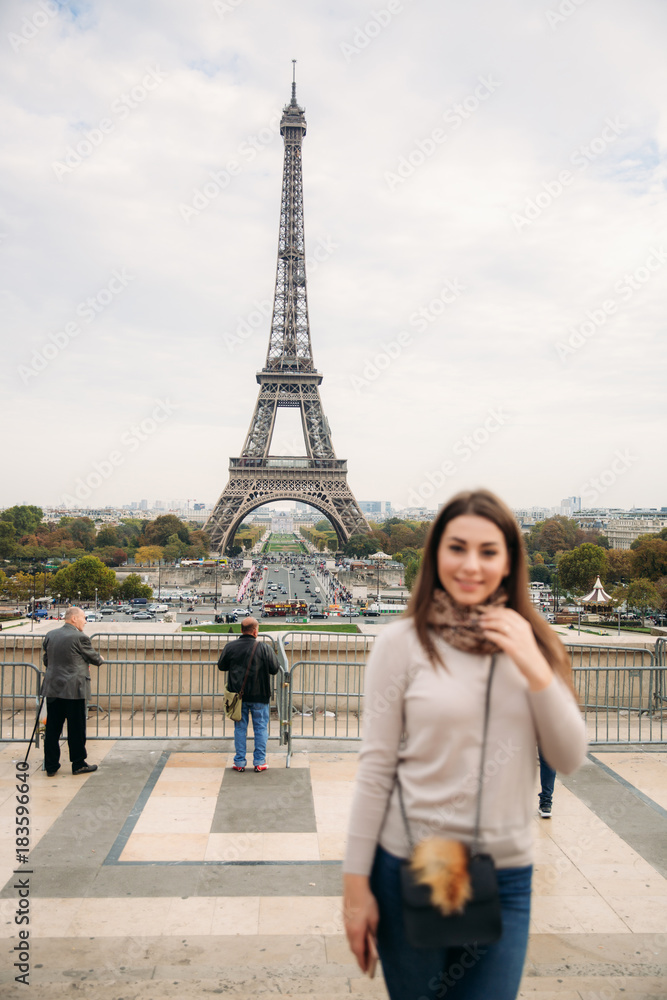 Beautiful girl posing to the photographer against the background of the Eiffel Tower. Autumn photosession. Sunny weather. Beautiful smile and makeup