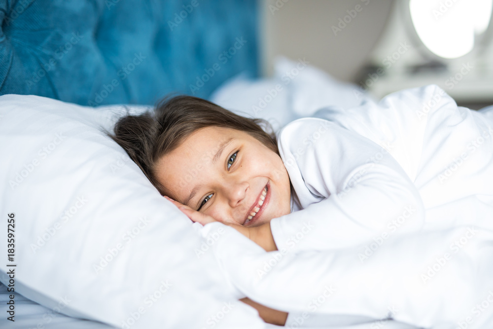 Close-up portrait of laughing little girl lying on bed with hand under pillow, looking at camera and smile. Good morning. Close-up portrait of laughing little girl lying on bed with hand under pillow, looking at camera and smile. Good morning.