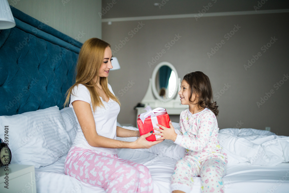 Happy mother and child daughter hugging and giving gifts in bed on Christmas morning Happy mother and child daughter hugging and giving gifts in bed on Christmas morning