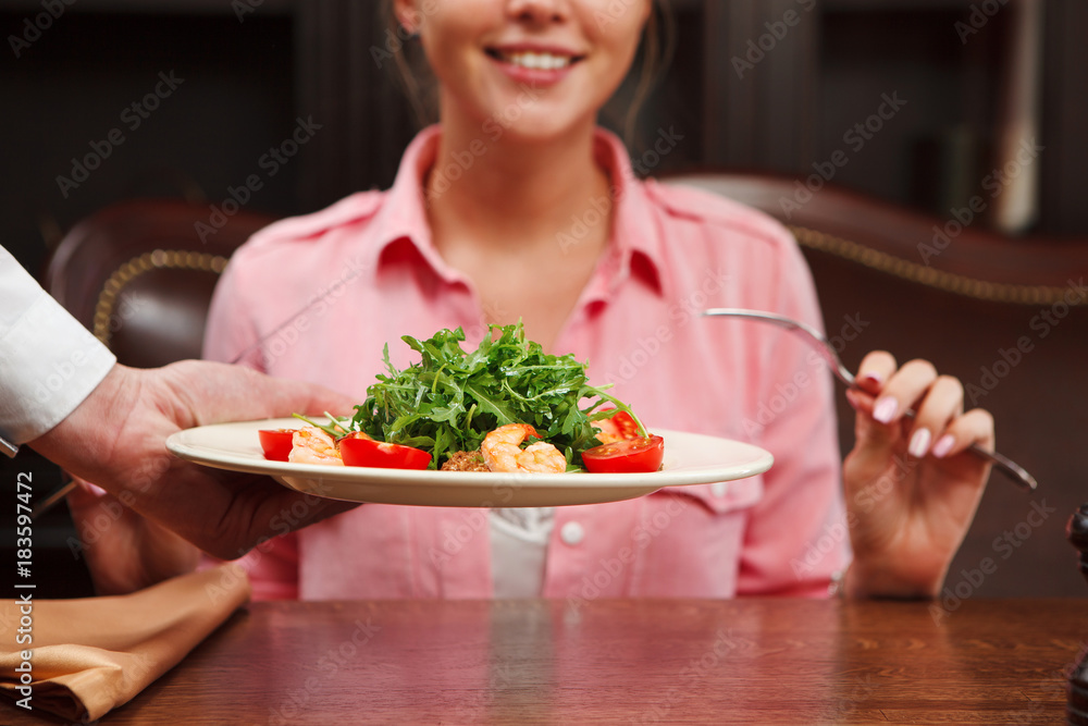 Waiter serve salad with green arugula leaves, tomato and shrimps