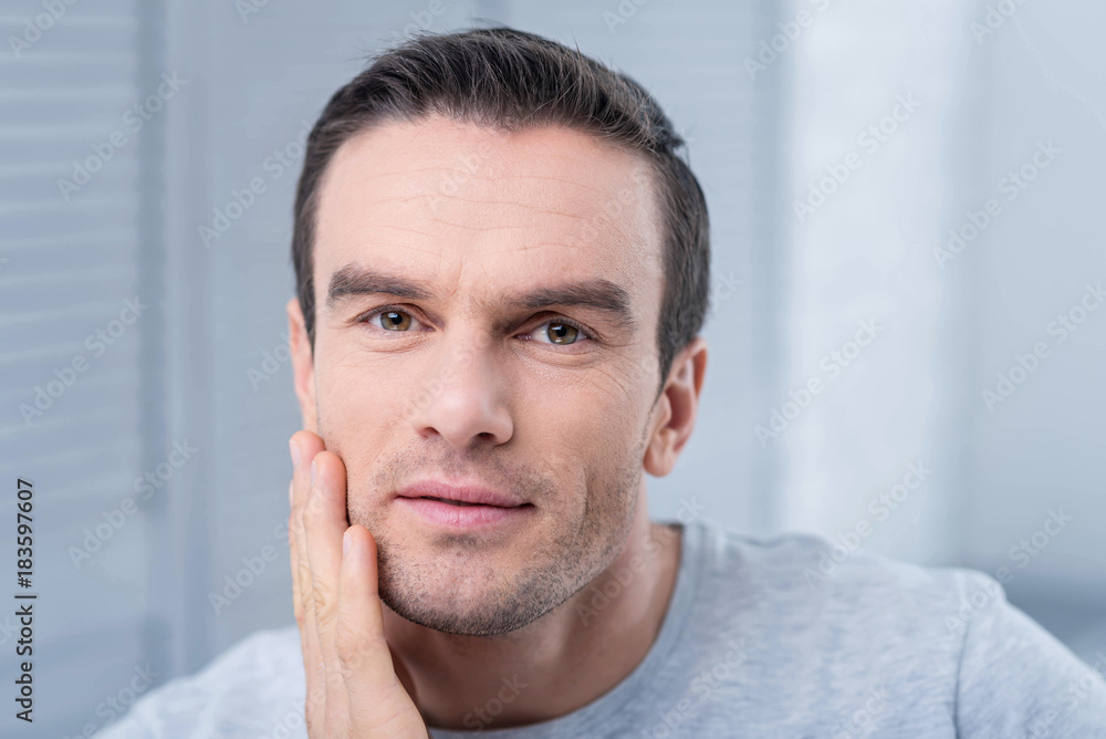 Accurate observation. Amazing young calm man touching his chick gazing at the camera while making conclusions Accurate observation. Amazing young calm man touching his chick gazing at the camera while making conclusions