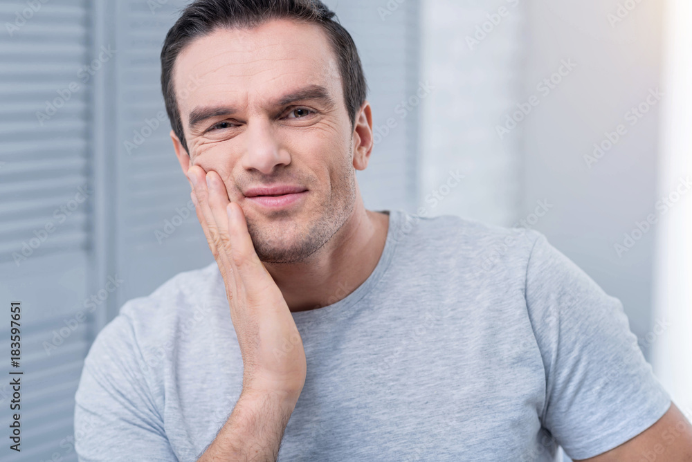 Morning irritation.  Perfect annoyed young man placing hand on the cheek after taking shower while wearing grey shirt 
