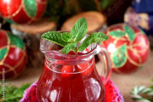 Hot cranberry tea in a glass jug surrounded by Christmas attributes