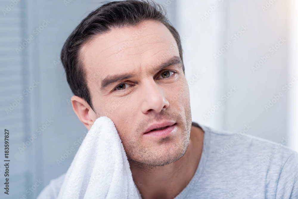 Fototapeta premium Work time. Pleasant attractive man putting white towel against the chin looking straight while posing on the light background
