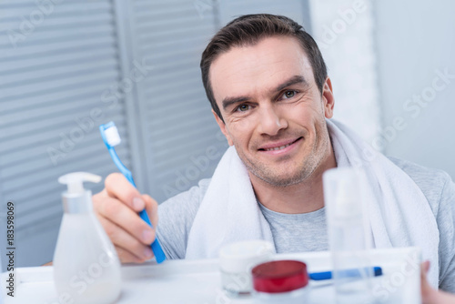 Smoothy skin. Gay young positive man shaving his beard while looking at the mirror and touching face 