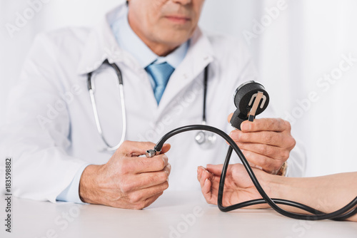 cropped image of male doctor measuring female patient pressure