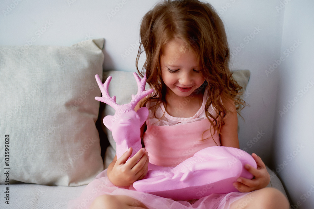 A lovely little girl 4 years old in a pink dress plays with pink deer. The atmosphere of childhood A lovely little girl 4 years old in a pink dress plays with pink deer. The atmosphere of childhood