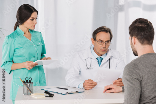 doctor talking to patient and nurse holding tablet