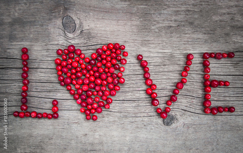 red ripe berries cranberries in the shape of a heart inscription love lie on rustic wooden background closeup. place for text. wooden old background. the concept of love.