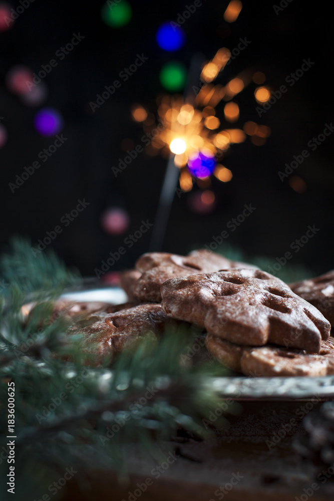 gingerbread cookies for the new year on a silver tray, New Year's lights, fireworks, fur-tree, cones, cinnamon on a wooden cutting board on a dark background gingerbread cookies for the new year on a silver tray, New Year's lights, fireworks, fur-tree, cones, cinnamon on a wooden cutting board on a dark background
