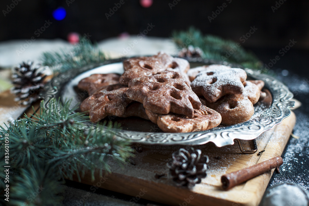 gingerbread cookies for the new year and Christmas on a silver tray, Christmas tree, cones, cinnamon on a wooden cutting board on a dark background gingerbread cookies for the new year and Christmas on a silver tray, Christmas tree, cones, cinnamon on a wooden cutting board on a dark background