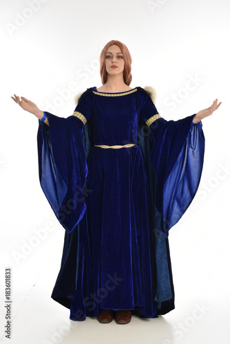 full length portrait of girl wearing long blue velvet gown and fur lined cloak, standing pose on white background.