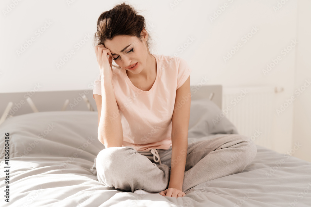 A lonely woman is crying alone, her mascara has flowed. She sits on a bed in a bright room. A lonely woman is crying alone, her mascara has flowed. She sits on a bed in a bright room.