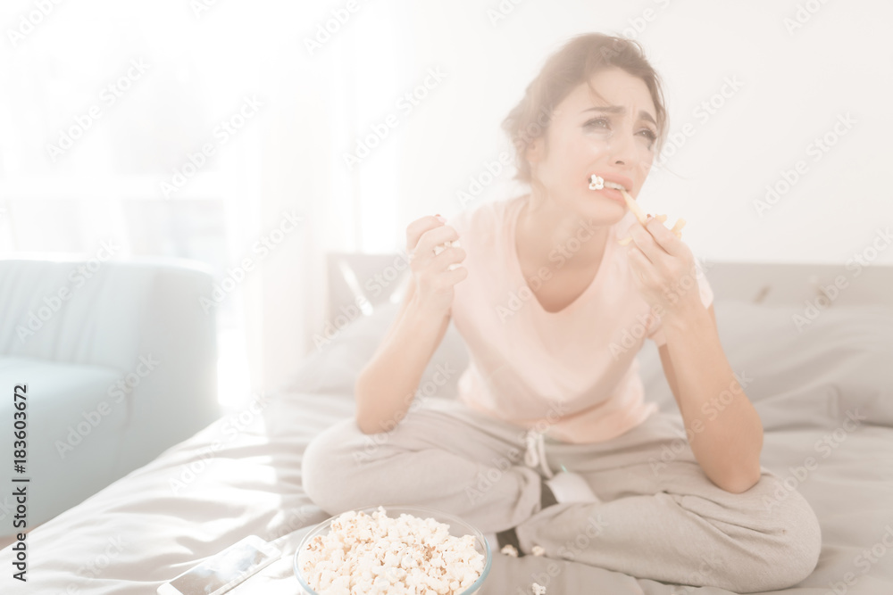 A lonely woman is crying alone, her mascara has flowed. She sits on a bed in a bright room. A lonely woman is crying alone, her mascara has flowed. She sits on a bed in a bright room.
