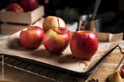 cooking of baked apples for New Year's holidays, Christmas tree and New Year's lights, honey and cinnamon on a wooden cutting board on a dark background