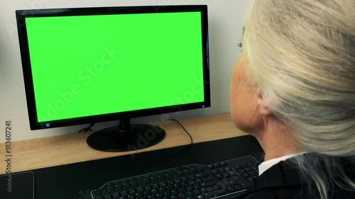 Old caucasian woman looks at monitor in home - green screen - closeup