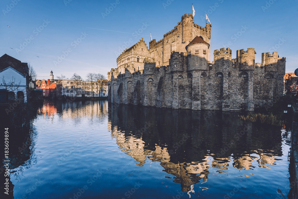 Gravensteen - historical medieval castle on water in Ghent, Flanders, Belgium. Castle of Counts stronghold reflected on canal in Gent city by sunset.