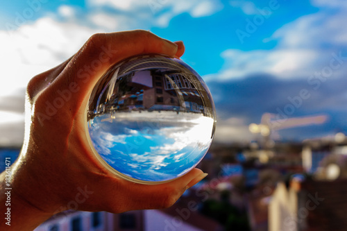 A hand holding a crystal ball for optical illusion. City as the background. Known as an orbuculum, is a crystal or glass ball and common fortune telling object. Performance of clairvoyance and scrying