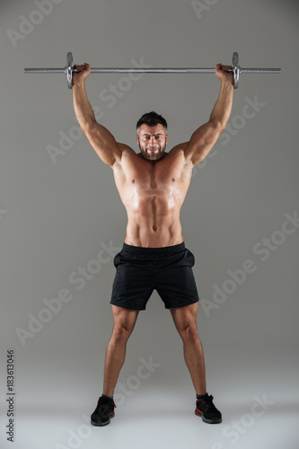 Full length portrait of a muscular serious shirtless male bodybuilder