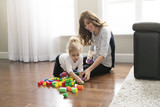 Mother and child daughter building from toy blocks at home