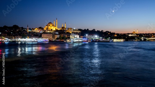 Istanbul cityscape with Suleymaniye mosque with tourist ships floating at Bosphorus at night