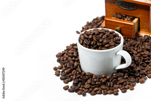 cup with coffee beans and handmilled coffee grinder on white table