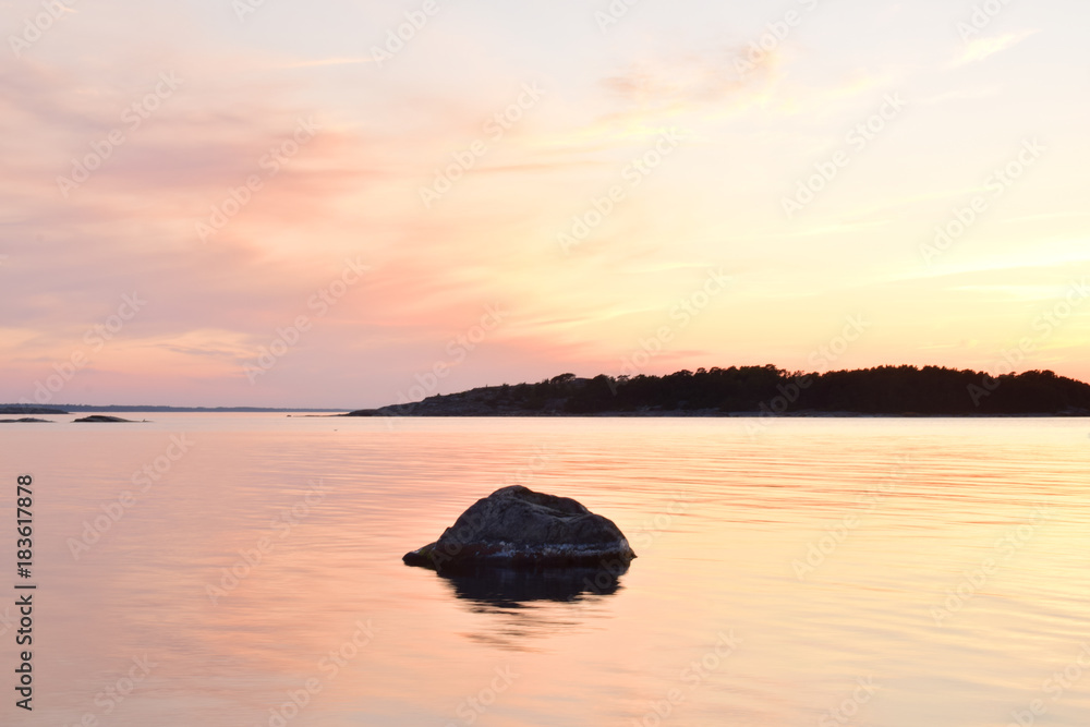 A calm, colorful and beautiful sunset with a lonely rock in the middle of the sea A calm, colorful and beautiful sunset with a lonely rock in the middle of the sea