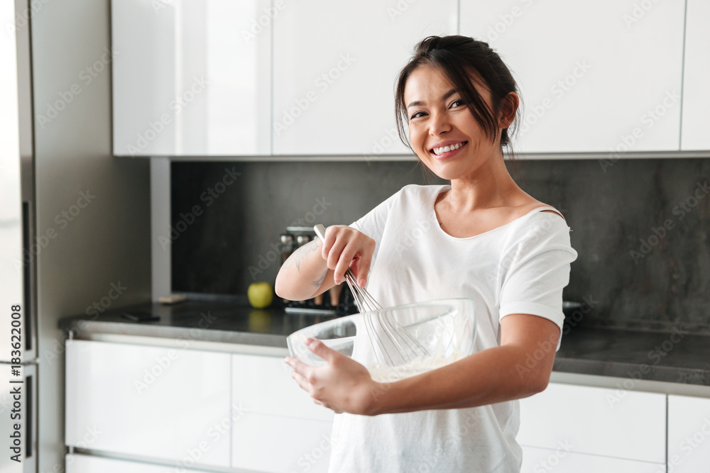 Smiling young woman standing at the kitchen in home Smiling young woman standing at the kitchen in home