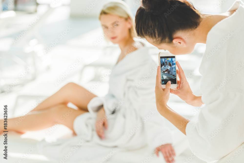young woman taking photo of her friend at spa center with smartphone young woman taking photo of her friend at spa center with smartphone