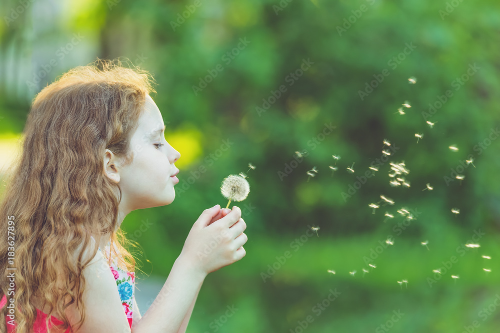 Cute girl blowing dandelion in spring park.