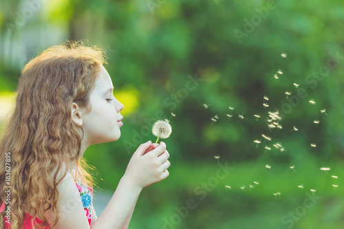 Cute girl blowing dandelion in spring park.