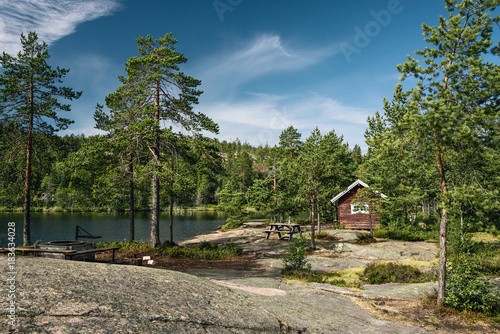 Tourist cabin of red color in a forest with lake. Blue sky with white clouds over the forest.