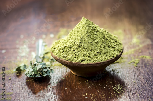 Raw organic powder of Henna,Lawsonia inermis in a clay bowl with its dry leaves on wooden surface. photo