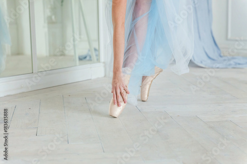 Beautiful legs of young ballerina who puts on pointe shoes at white wooden floor background, top view from above with copy space. Ballet practice. Beautiful slim graceful feet of ballet dancer.