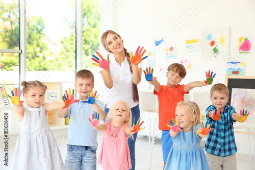 Children and teacher with hands in paint at art lesson photo