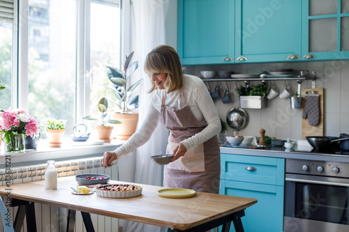 Pretty senior Caucasian woman making fruit pie at kitchen.