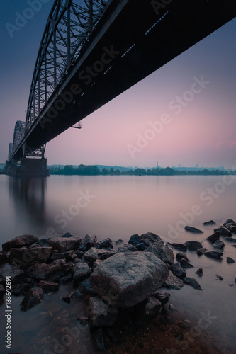 Beautiful dusk landscape with bridge over river and stones in the water on foreground. Long exposure.