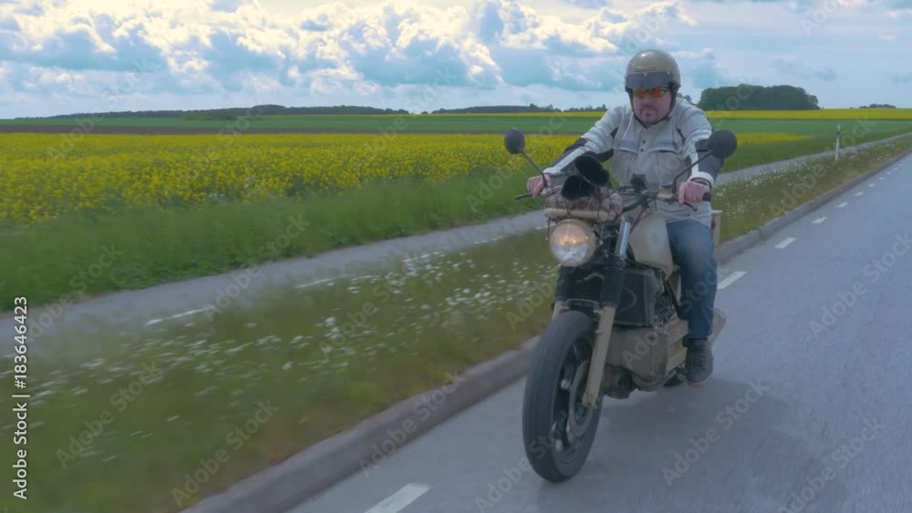 Male biker rides his custom motorbike down an open county road Male biker rides his custom motorbike down an open county road