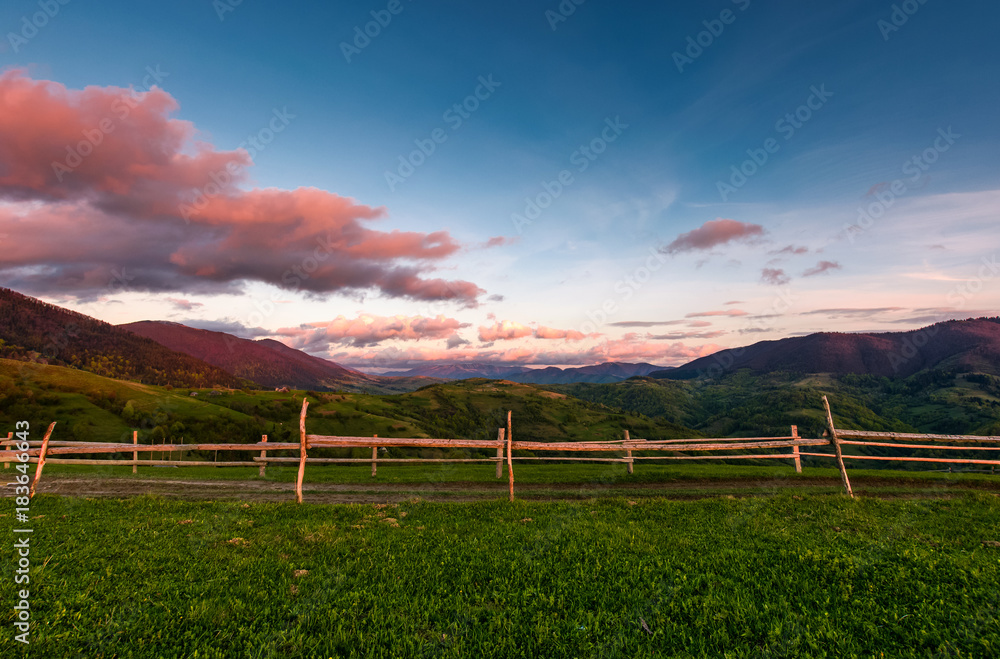 wooden fence on a grassy hill at sunset. beautiful rural scenery with reddish clouds over the mountain ridge