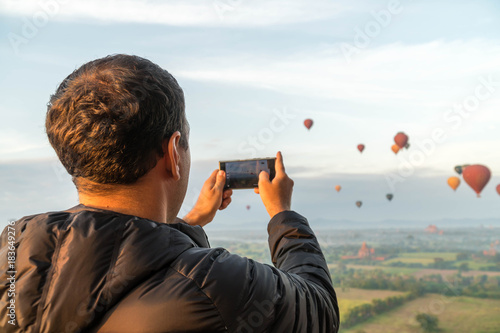 Male Tourist Taking Mobile Photo of Hot Air Balloons in Bagan, Myanmar