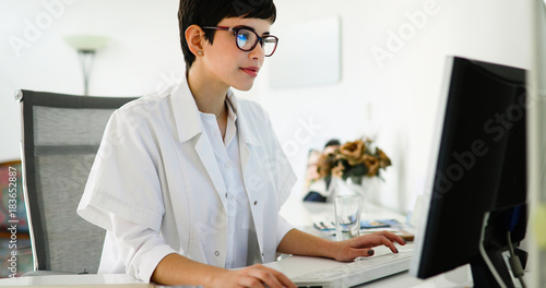 Beautiful female doctor typing receipt for patient