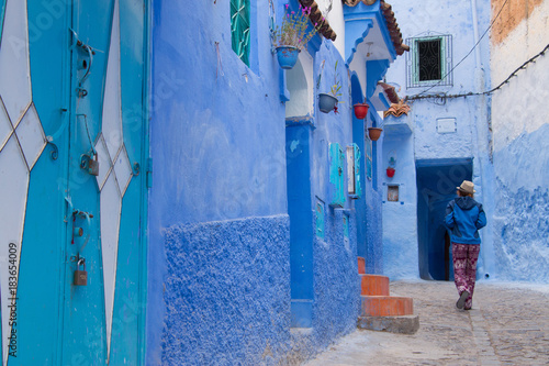 Tourists walking in moroccan courtyard in Chefchaouen blue city medina in Morocco. Traditional architectural details in Blue town Chaouen. Typical blue walls and colorful flower pots. © sefoma