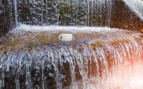 A white coffee cup is placed in the middle of a stream of waterf photo
