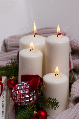 Four white glowing advent candles with christmas decorations on silver tray