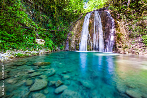 Waterfall in a green spring forest surrounded by stones, clear turquoise water on an impressive natural landscape. 33 Waterfalls, Sochi, Russia.