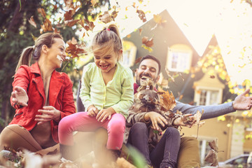 Happy family playing with leaves at backyard .