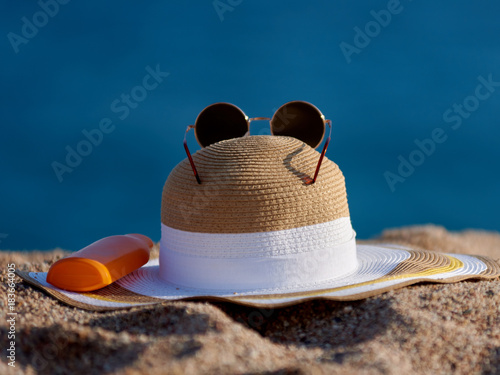 Bonnet hat, sunglasses and bottle of sunscreen against the sea.