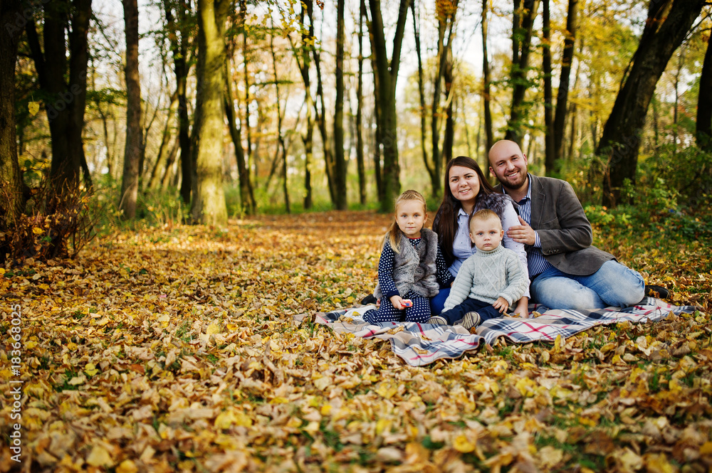 Happy caucasian family of mom dad and little girl with boy sitting on plaid at majestic autumn fall forest. Happy caucasian family of mom dad and little girl with boy sitting on plaid at majestic autumn fall forest.