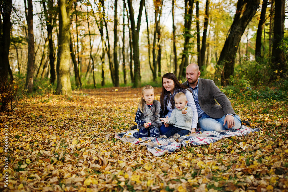 Happy caucasian family of mom dad and little girl with boy sitting on plaid at majestic autumn fall forest. Happy caucasian family of mom dad and little girl with boy sitting on plaid at majestic autumn fall forest.